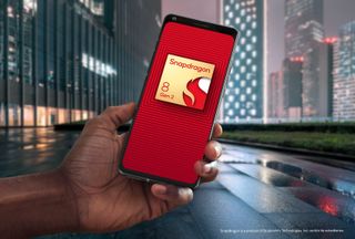 En pressbild för Qualcomm Snapdragon 8 Gen 2, där chippet visas upp mot en röd bakgrund på en mobilskärm som hålls upp mot en stadsbakgrund under kvällstid.