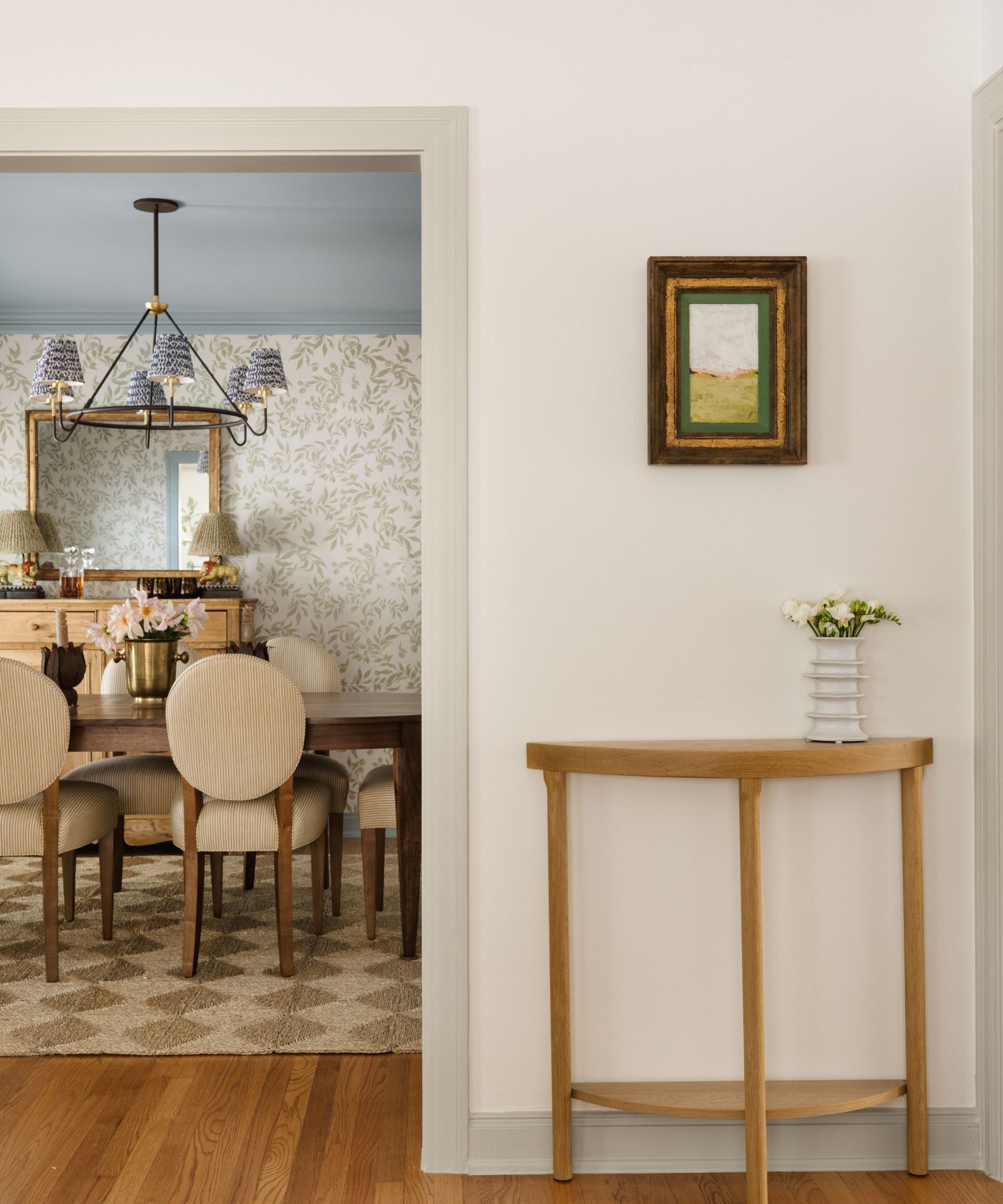 A living room with warm white walls, light gray trimwork, a wooden console table, and a doorway leading into a dining room.