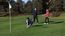 A golfer lines up a putt with two golfers signalling behind him