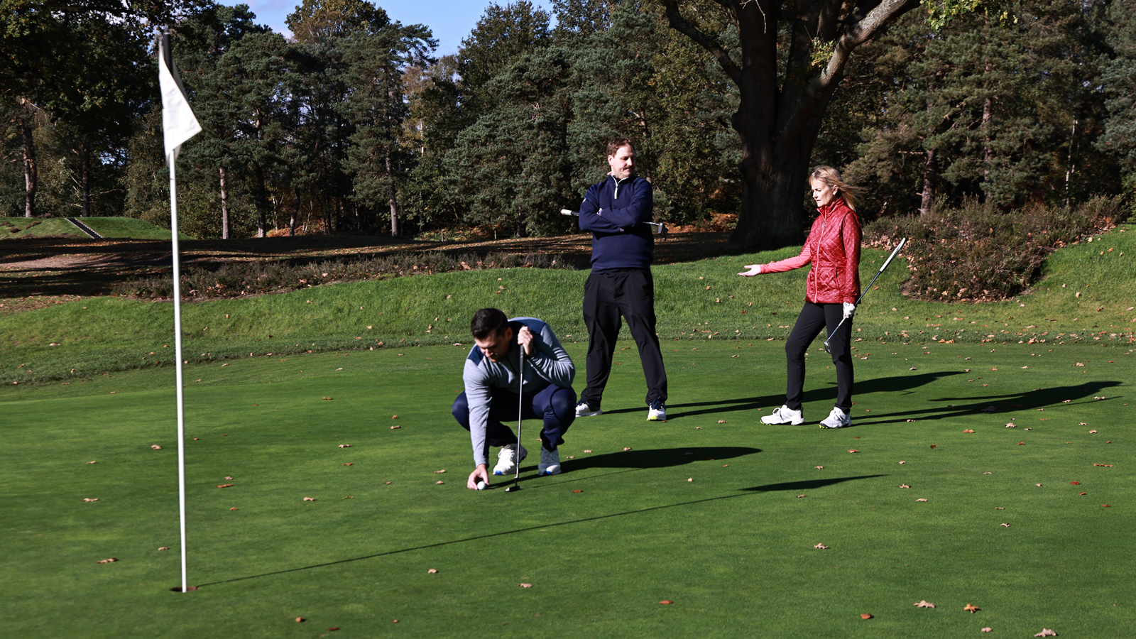 A golfer lines up a putt with two golfers signalling behind him