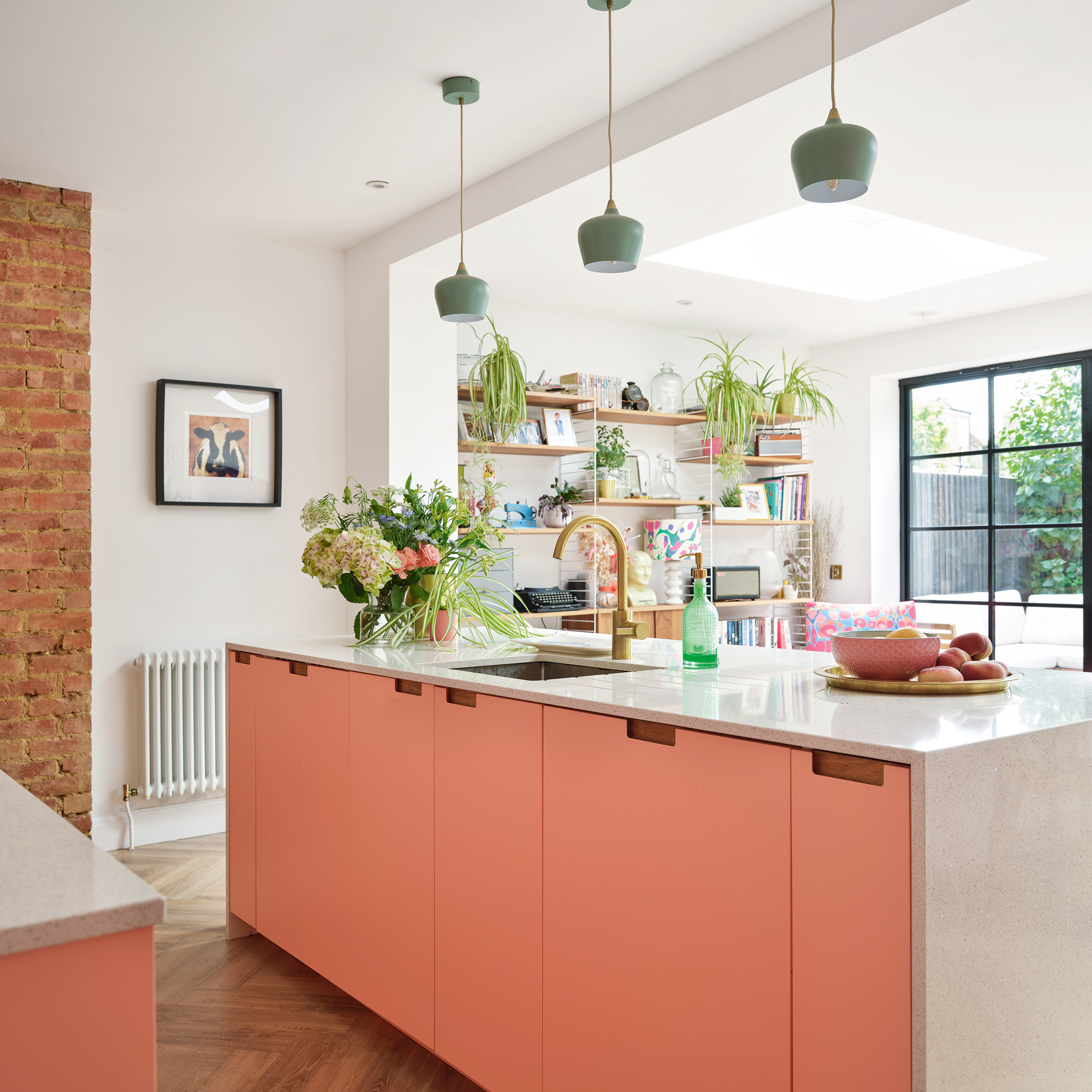 pink kitchen with a pink kitchen island, an exposed brick wall, a trio of pendant lights and mid century shelving beside a patio door