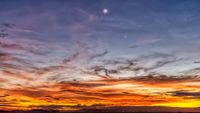 a fiery orange sunset sky with the moon upper center and Venus to the lower right.