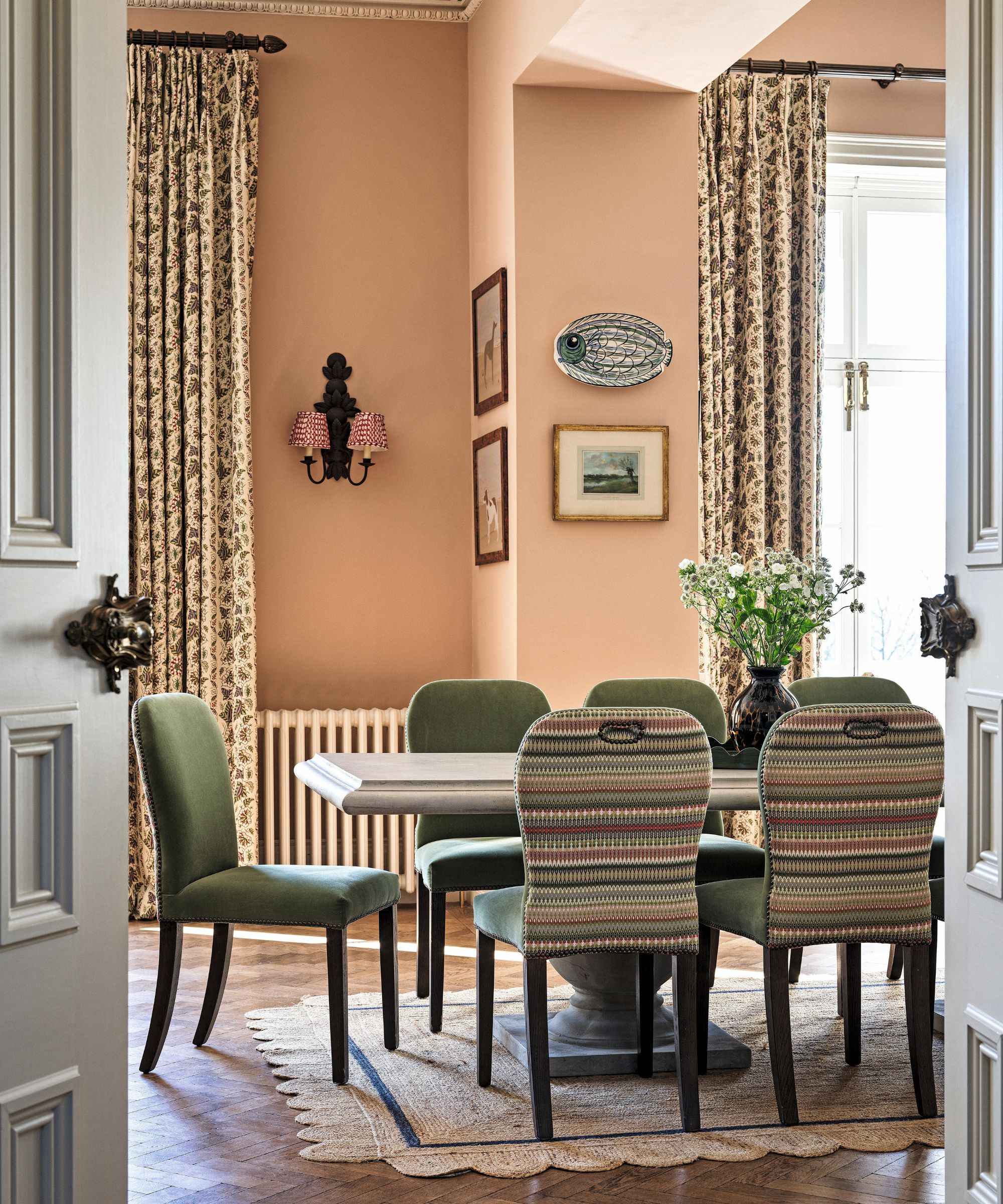 a pink dining room in a grand english home with green dining chairs and a scalloped rug