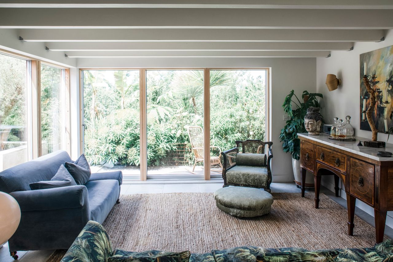 A garden room with white beams and large picture windows leading out to a garden full of tropical plants