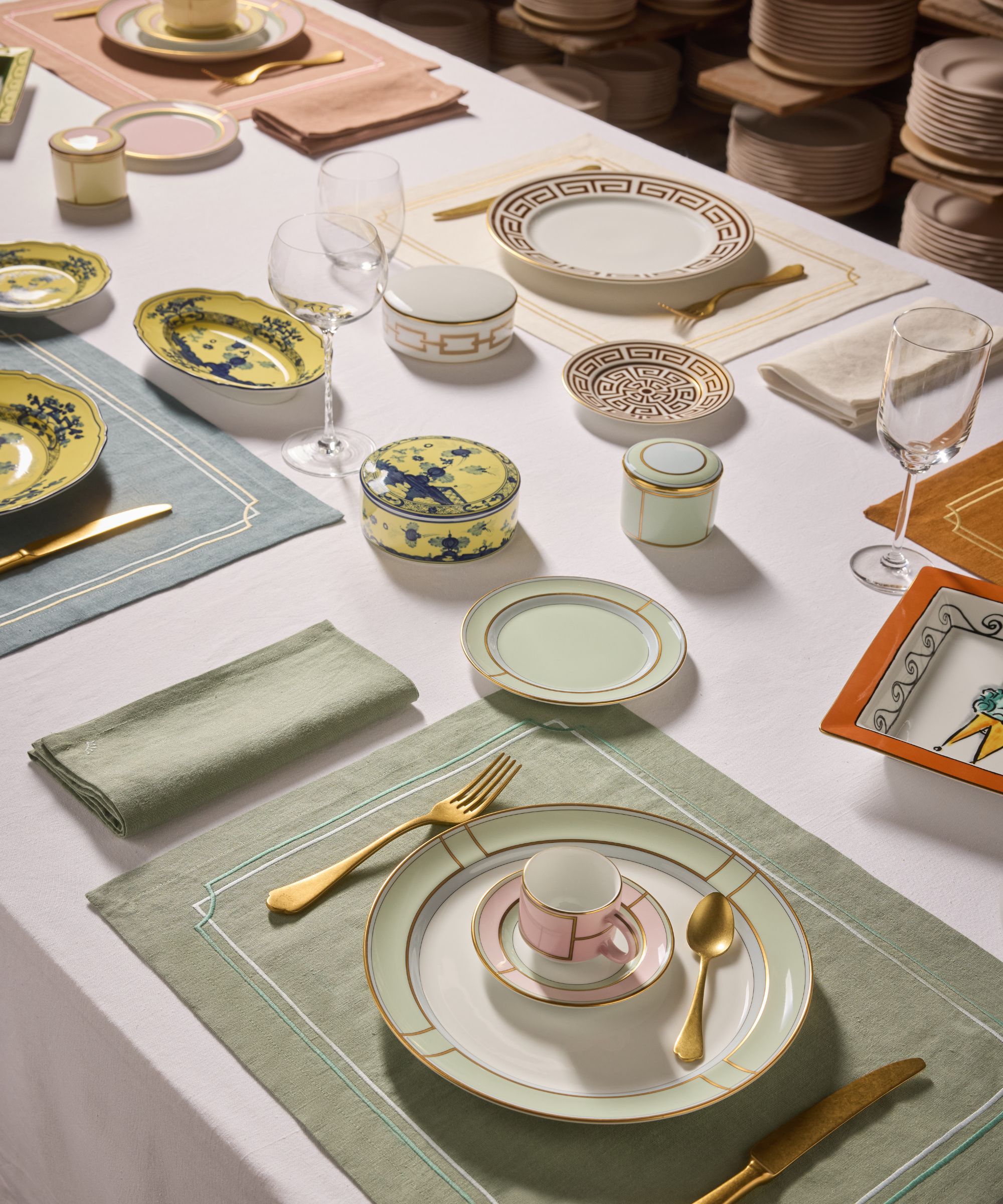 table set with Ginori 1735 plates with green, blue, pink, and cream linen placemats, gold cutlery, and glassware