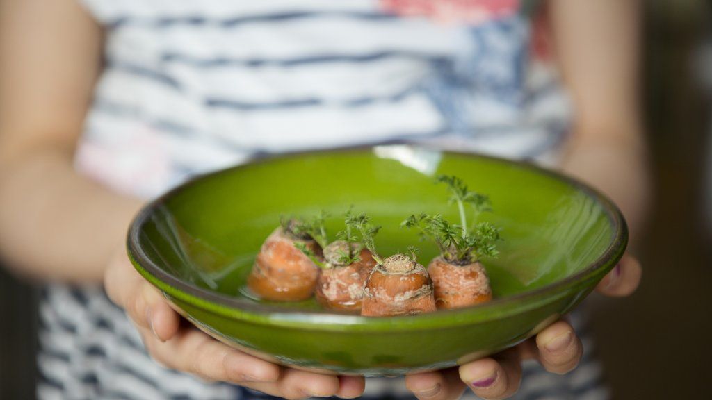 A child holds a green plate of carrot tops