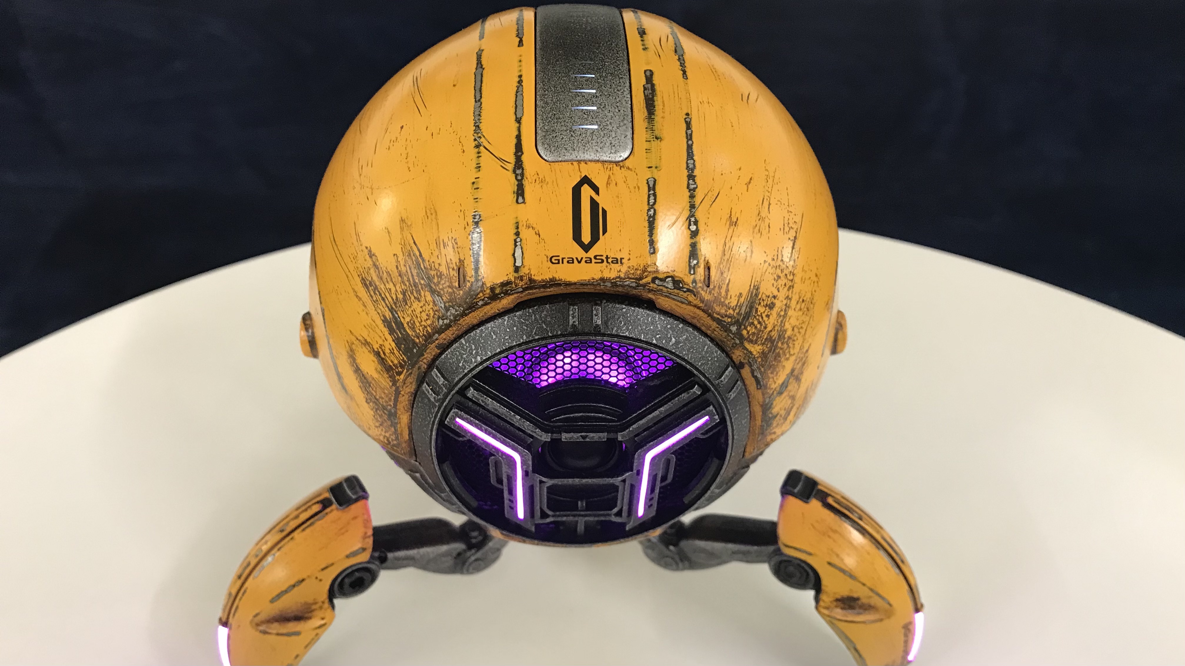 GravaStar Mars Pro in War Damaged Yellow on white table with lights glowing purple