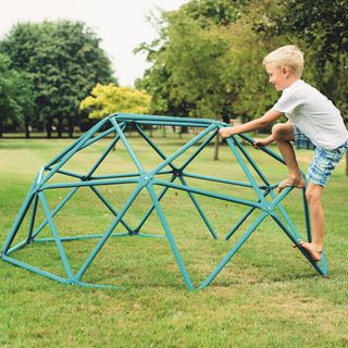 a boy climbing on a green climbing dome frame in the middle of a large open green park