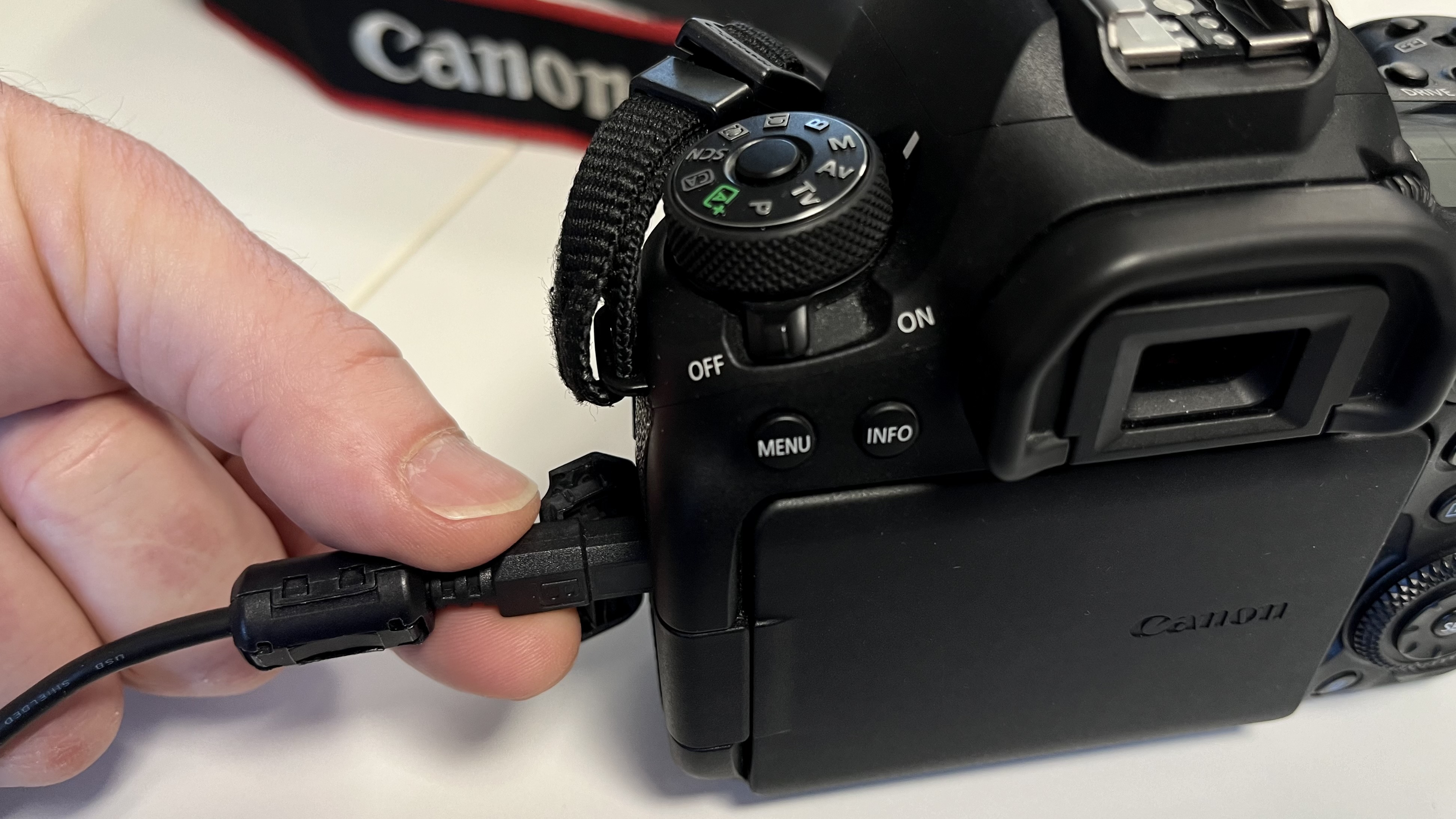 Hand pushing USB cable into the micro USB port of a Canon EOS 6D Mark II