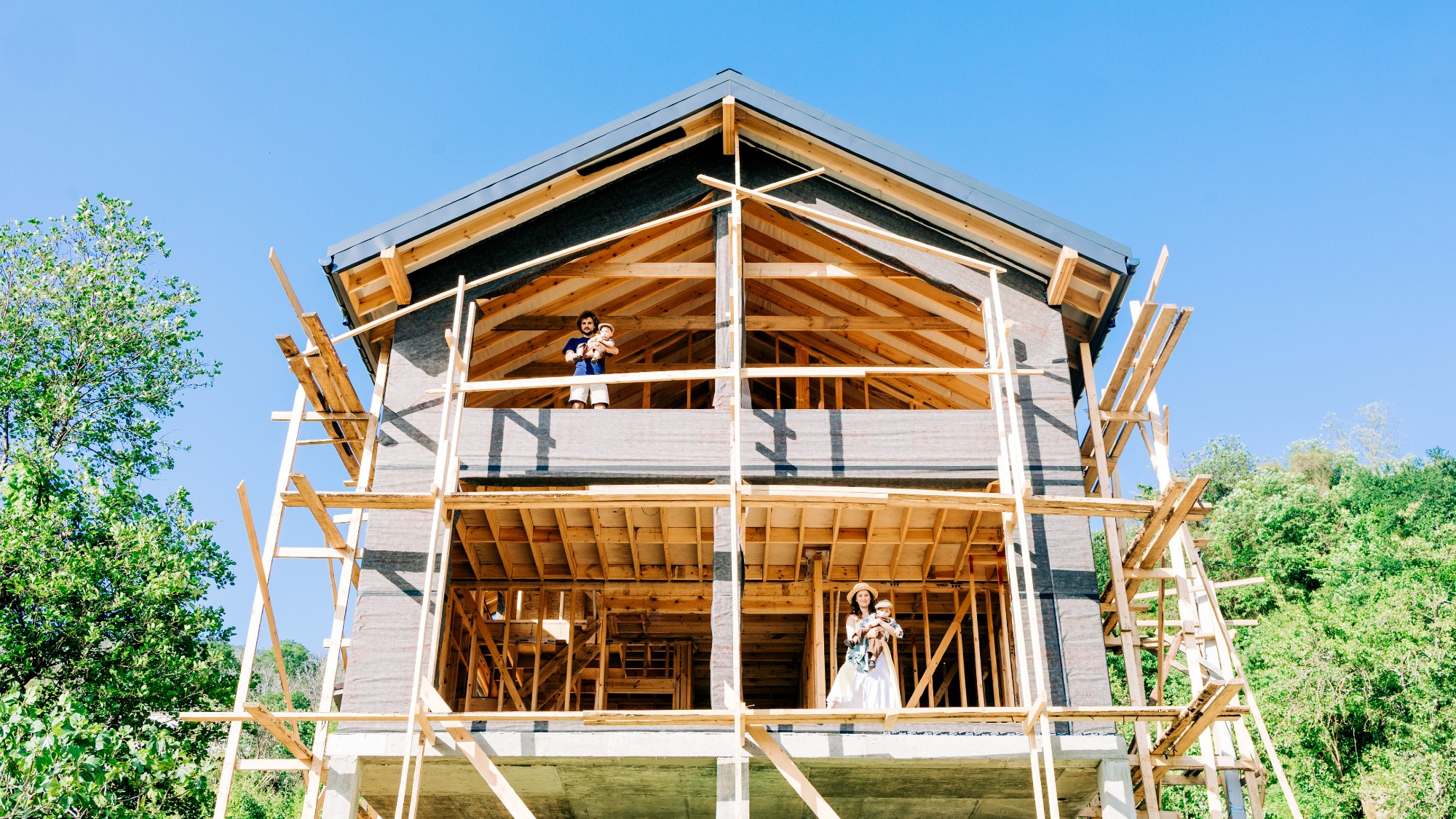 Couple standing inside of a brand new house being built, holding their kids 