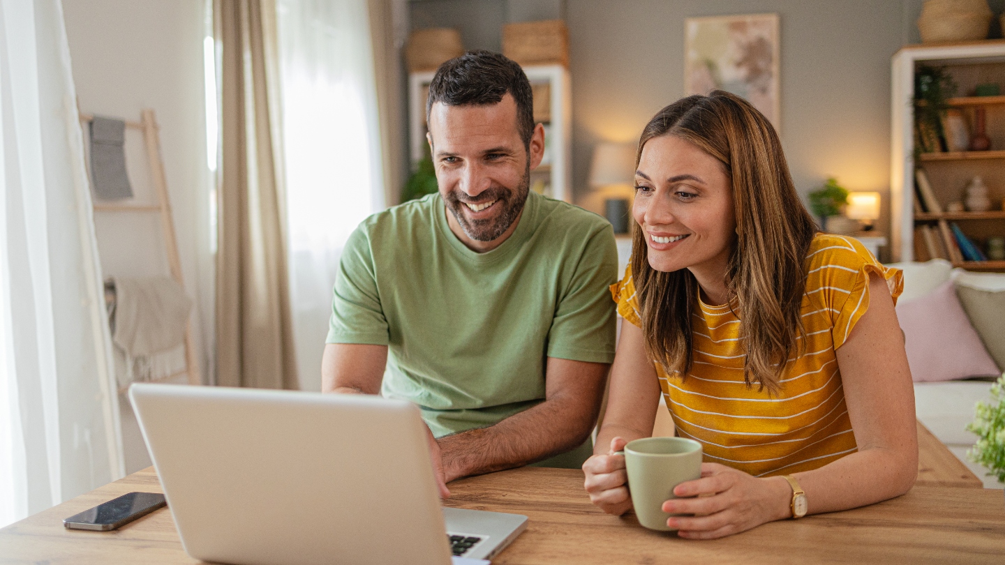 Young couple sitting at table smiling at laptop screen