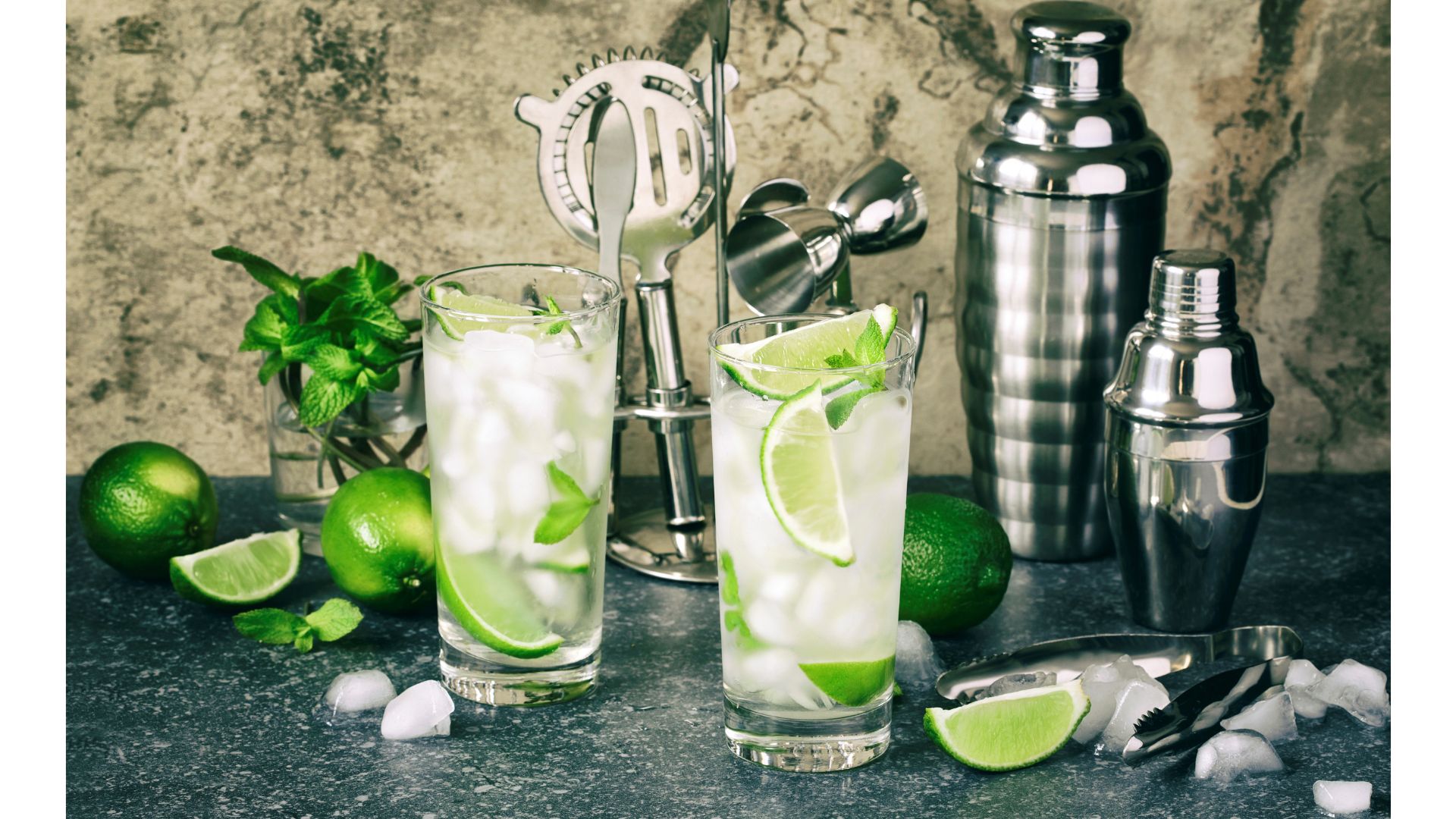 Mojito cocktail with lime and mint in glass on a stone table. Bar tools and ingredients for cocktails with ice around them