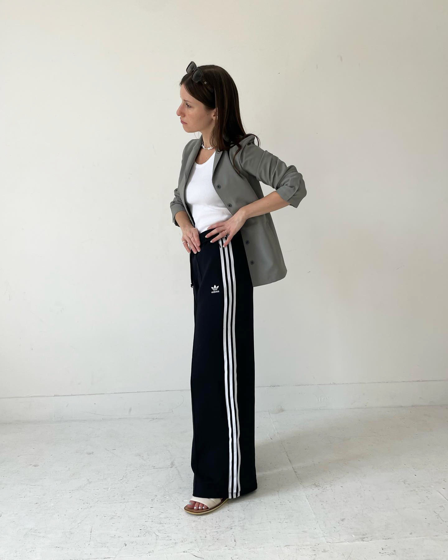 fashion influencer Laura Reilly poses in a gray blazer, white tank top, Adidas striped track pants, and slide sandals