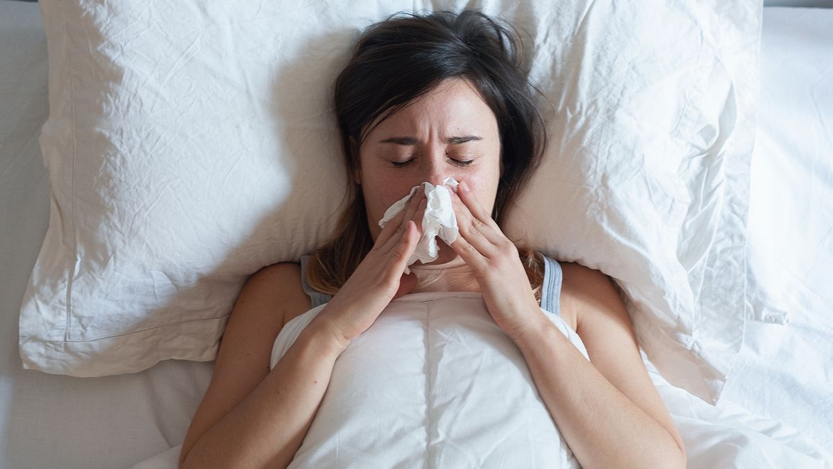 A woman lying in bed with a cold, blowing her nose