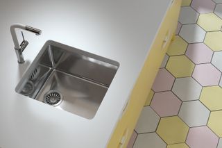 undermount stainless steel sink in a white worktop with pink and yellow floor tiles below
