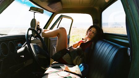 Zendaya's Rue smiling as she sits in a car with her feet on the steering wheel in Euphoria season 3