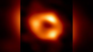 the black hole at the milky way galaxy's heart is seen as a bright, fuzzy orange donut-shaped object against the blackness of space.