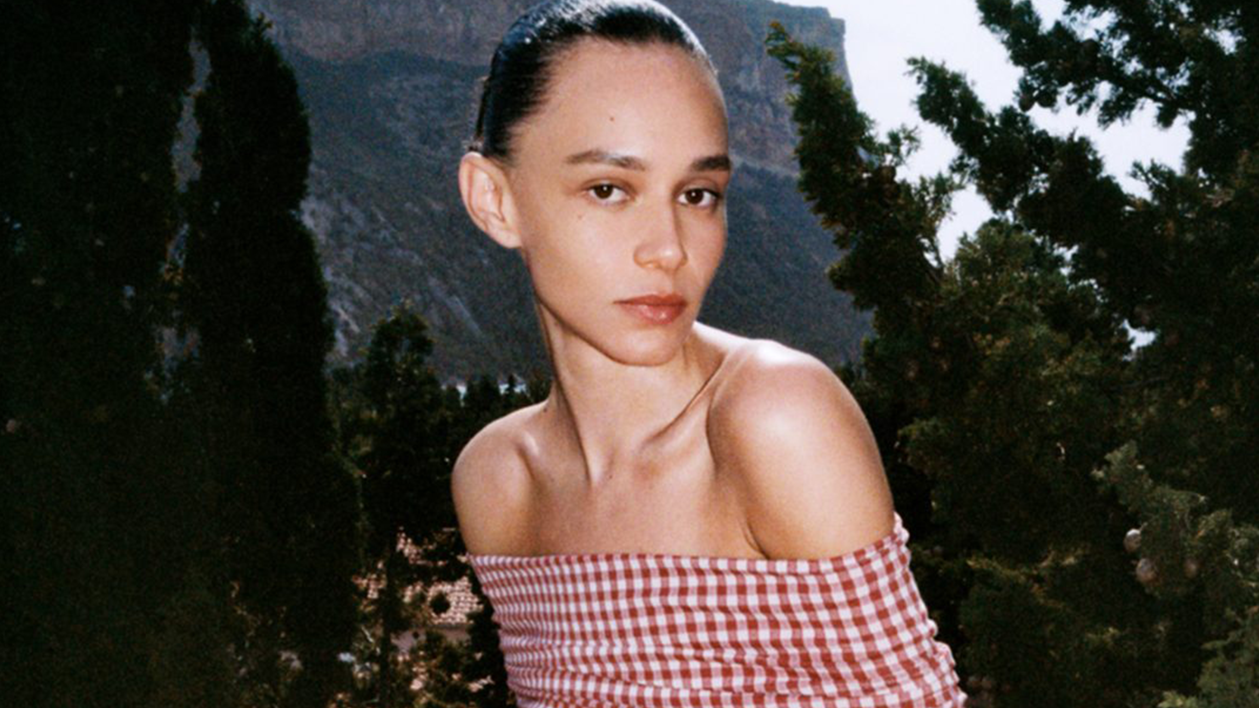 Model wearing an Alaia gingham off-the-shoulder midi dress.