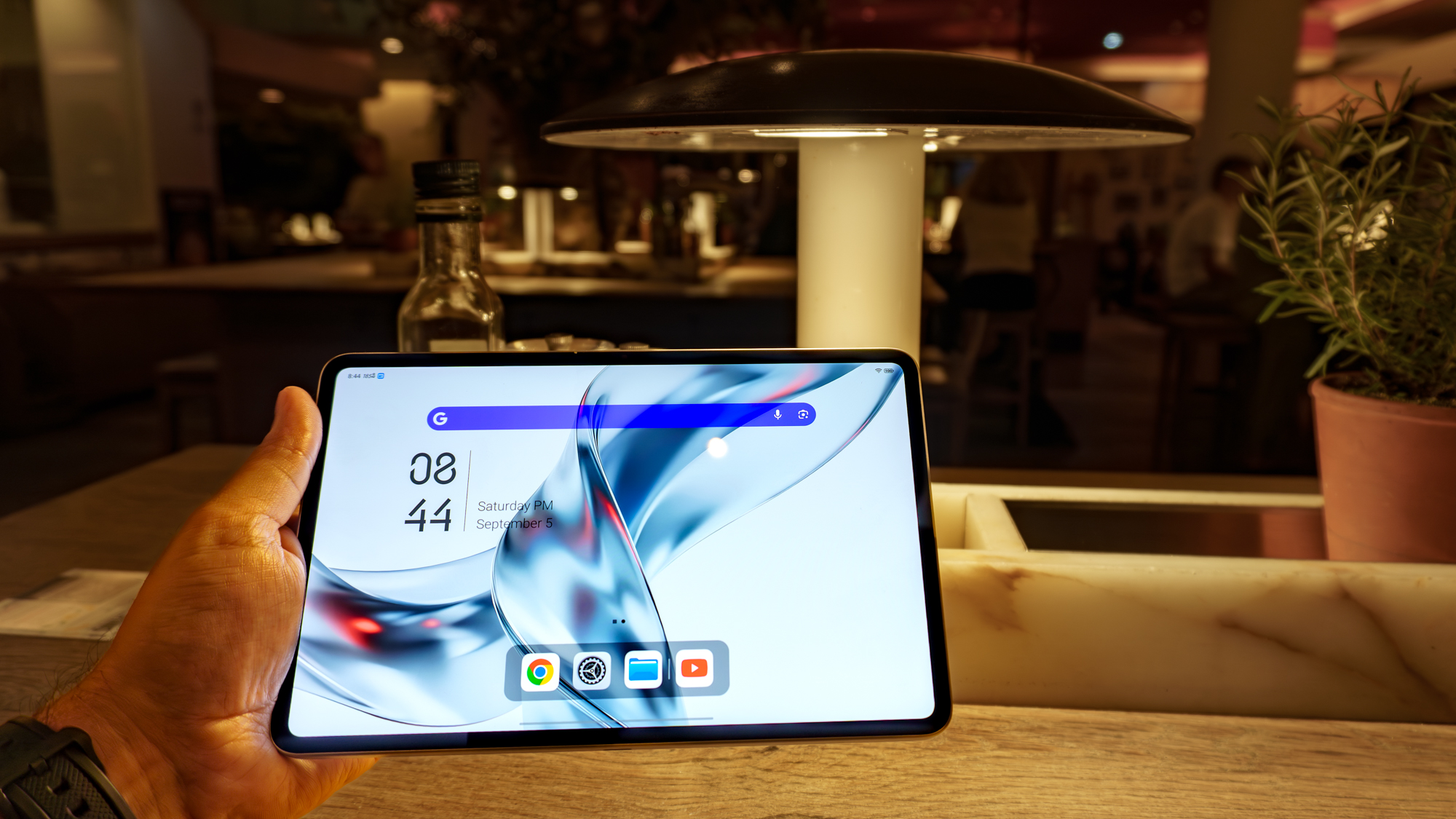 A person holding the RedMagic Astra 2 gaming tablet in portrait mode at a dark restaurant