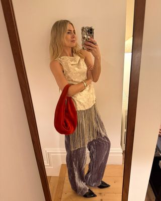 A influenciadora de estilo britânico Lucy Williams posa para uma selfie no espelho com uma capa prateada para iPhone vestindo uma roupa de festa com blusa sem mangas com franjas da Sea, bolsa de veludo vermelho e calça de veludo roxa