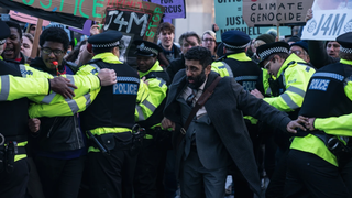 Solicitor Sam Malik (played by Adeel Akhtar) holds back a crowd of protestors waving placards in a scene from BBC's TV drama Showtrial season 2