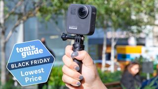The GoPro Max on a selfie stick in hand, with an out of focus background.