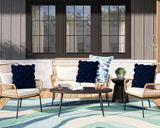 Origin 21 Brynlee 4-Piece Wicker Patio Conversation Set in back yard by big black windows sitting on top of blue rug with blue cushions