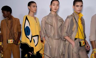 Models wear brown suede blazer and trousers, yellow poncho, beige jacket, top and trousers, and beige jacket and trousers with yellow top