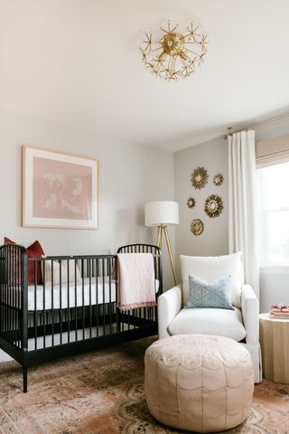 gender neutral nursery with black cot, armchair, footstool, sunburst mirrors, artwork, neutral scheme
