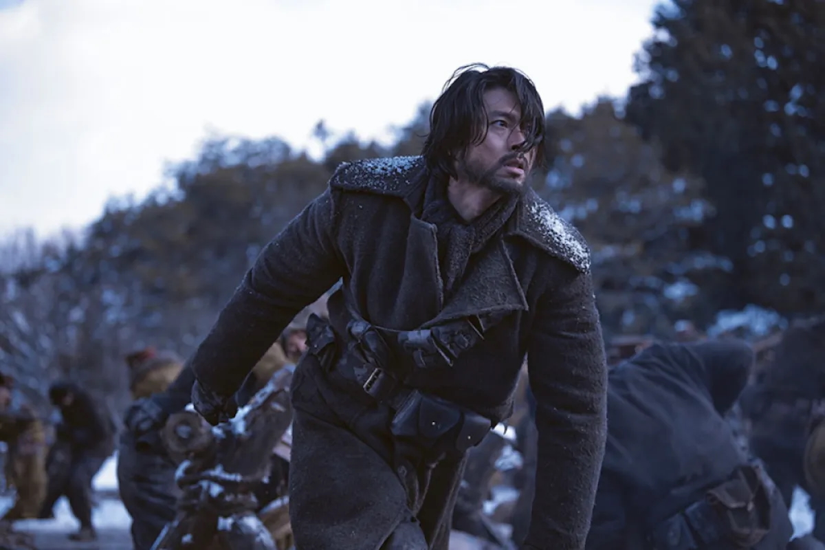 A man (Hyun Bin as Ahn Jung-geun) walks in front of men fighting in a snowy forest, in the Korean movie 'Harbin.'
