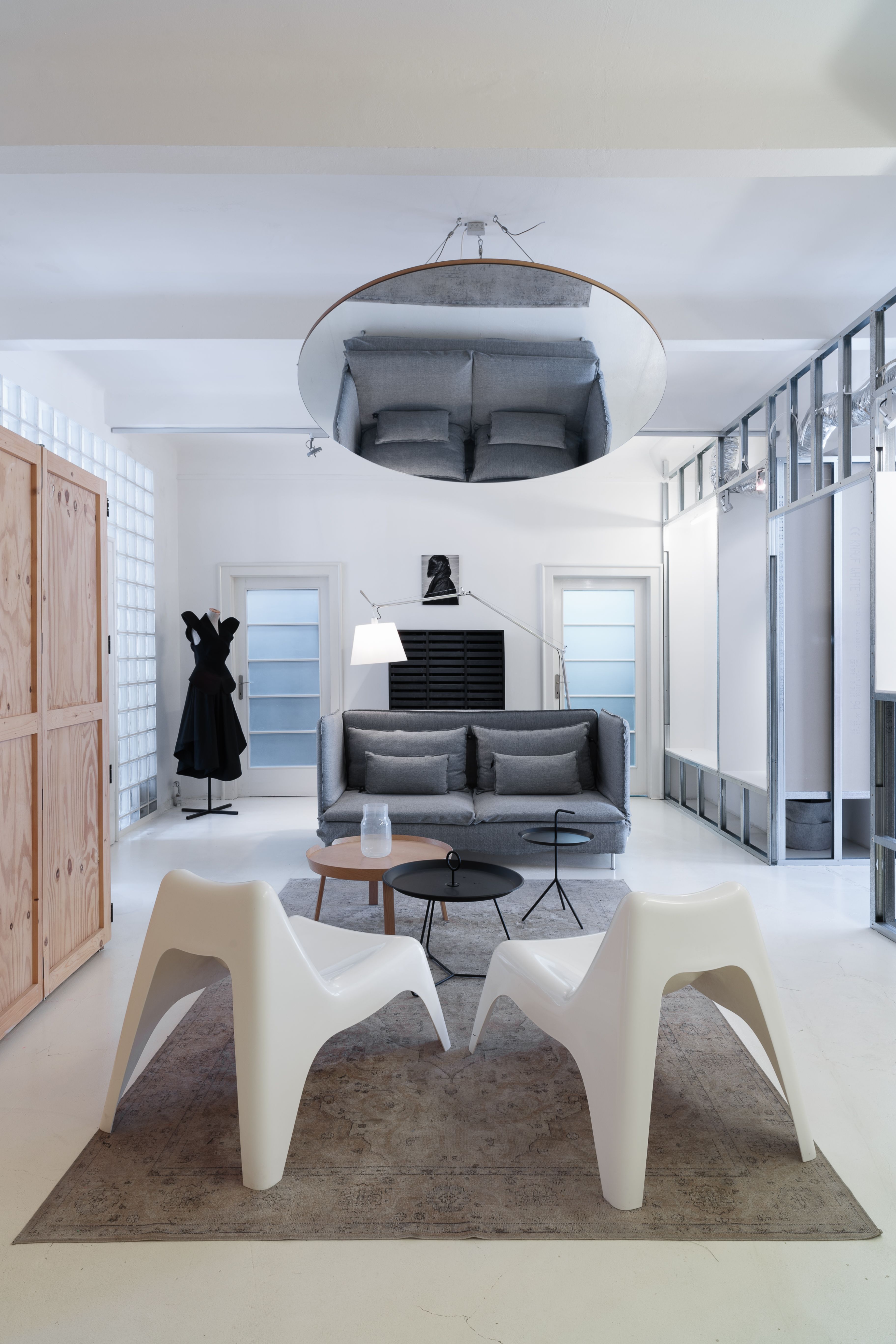 A minimalist fashion atelier with sculptural, monochromatic furniture, wood, iron, and textile accents, and a black dressed sitting on a mannequin on the left.