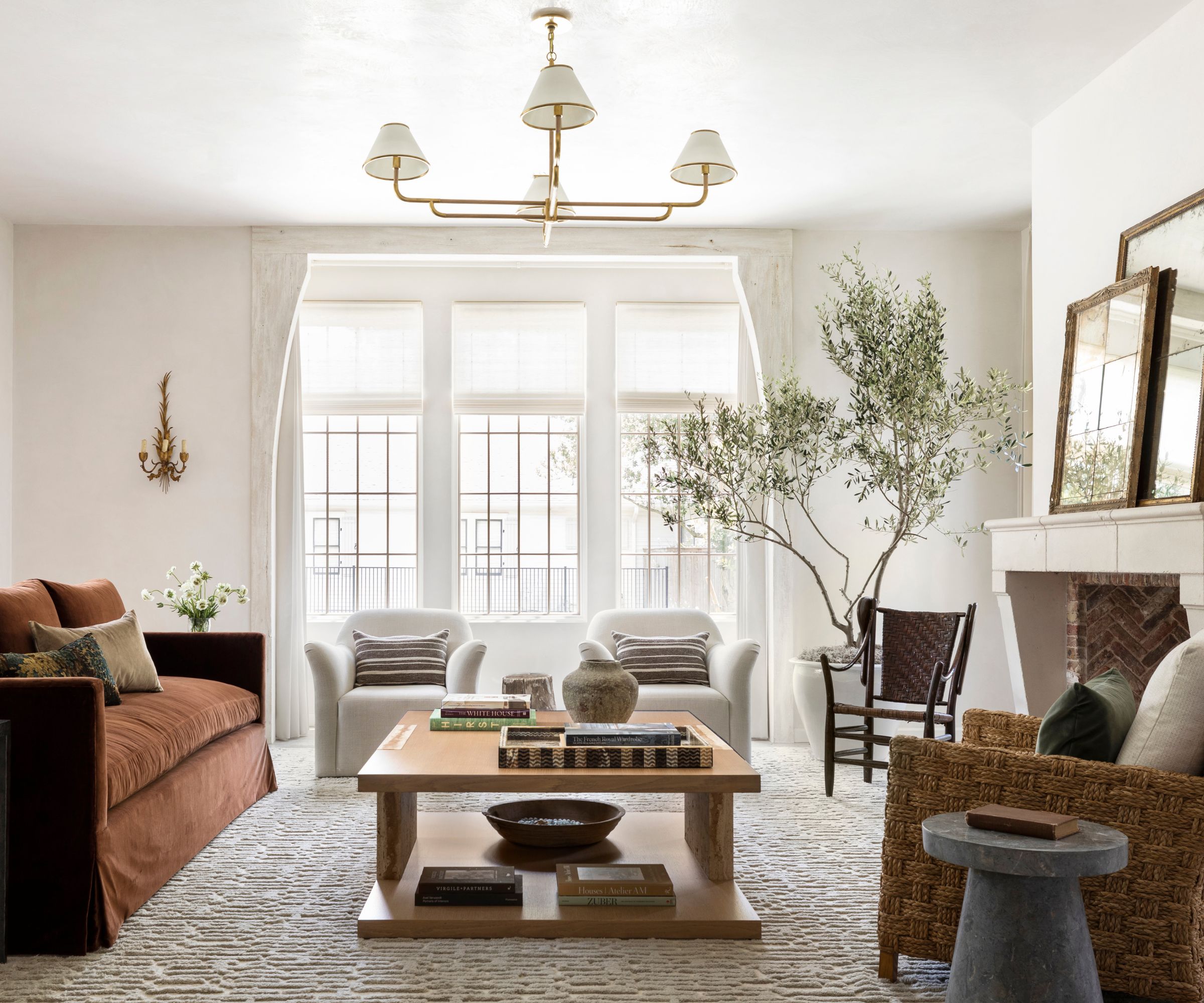 A light and airy living room with soft white walls, three side-by-side windows, a neutral rug, a brown linen sofa, two cream armchairs, and a wooden coffee table.