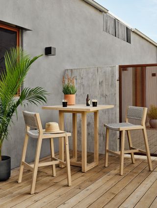 two bar chairs and a tall wooden bar table on a wooden decking with potted plants
