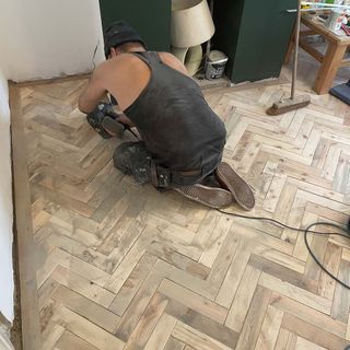 during view of wooden floor renovation with man on his knees operating a grinder