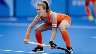 Xan de Waard, in orange vest, shorts and socks, crouches with her stick during a Netherlands women&#039;s hockey match at the 2024 Paris Olympics Games. 