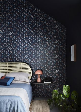 An dark painted bedroom has a wallpapered feature wall