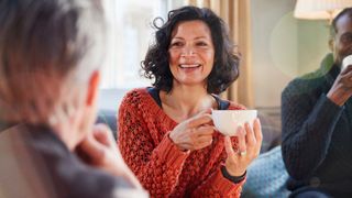 Woman holding coffee cup and smiling, looking at friends after learning how to make friends as an adult