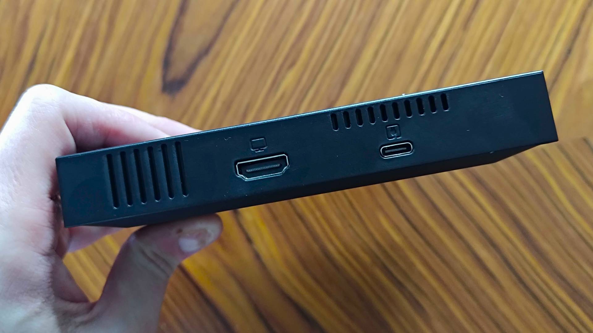 Hand holding G'AIM'E Time Crisis console with back ports facing camera.