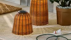 Pair of woven outdoor lanterns styled on a back porch alongside a potted plant and badminton accessories.