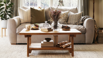 brown coffee table stacked with books and ornaments in front of cream sofa