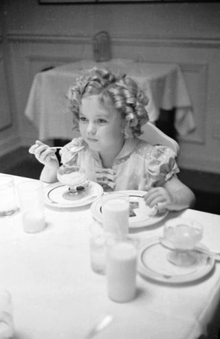Young Shirley Temple eating at table, black & white still