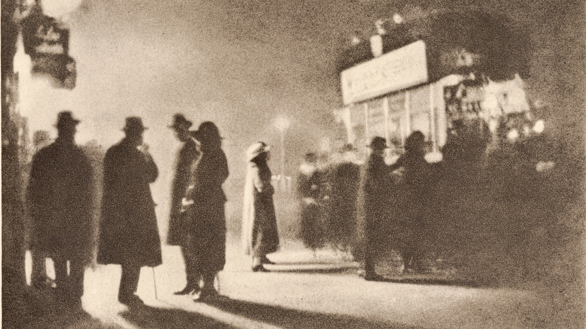 A grainy photogravure of several coated, hatted figures standing in silhouette on a pavement, their long shadows stretching across the ground beneath a glowing street sign.