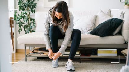 Woman sitting on sofa, tying shoelaces on trainers after trying to put a Fitbit on ankle for fitness tracking