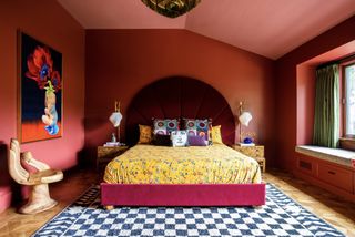 red color drenched bedroom with yellow sheets and throw pillows, a large artwork and hand-shaped seat, and velvet red headboard