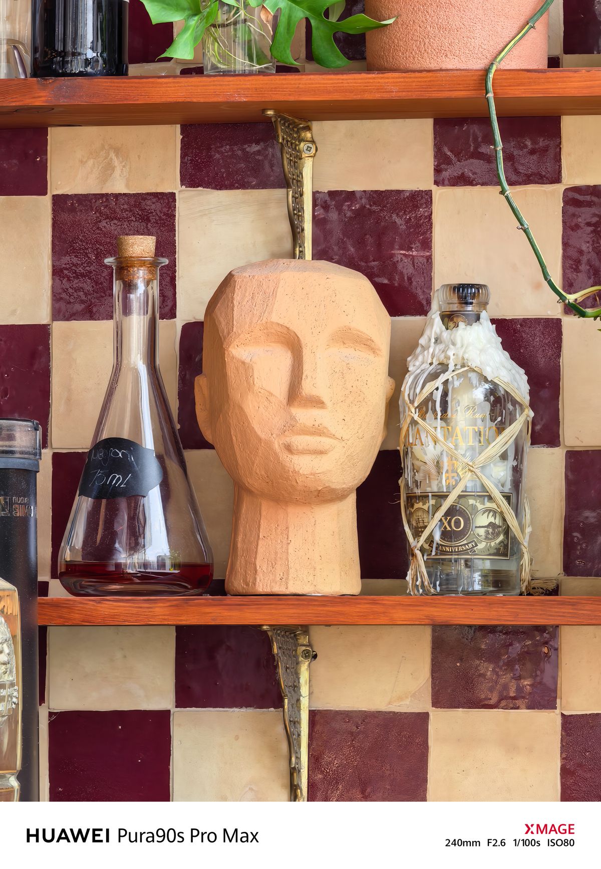 Decorative terracotta head displayed between glass bottles on a shelf against red and cream tiles.