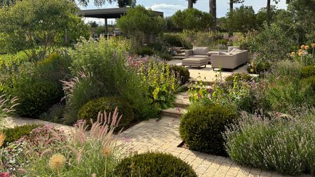 split level garden design featuring planting beds, raised patio area with garden furniture and pergola, all linked by brick paths