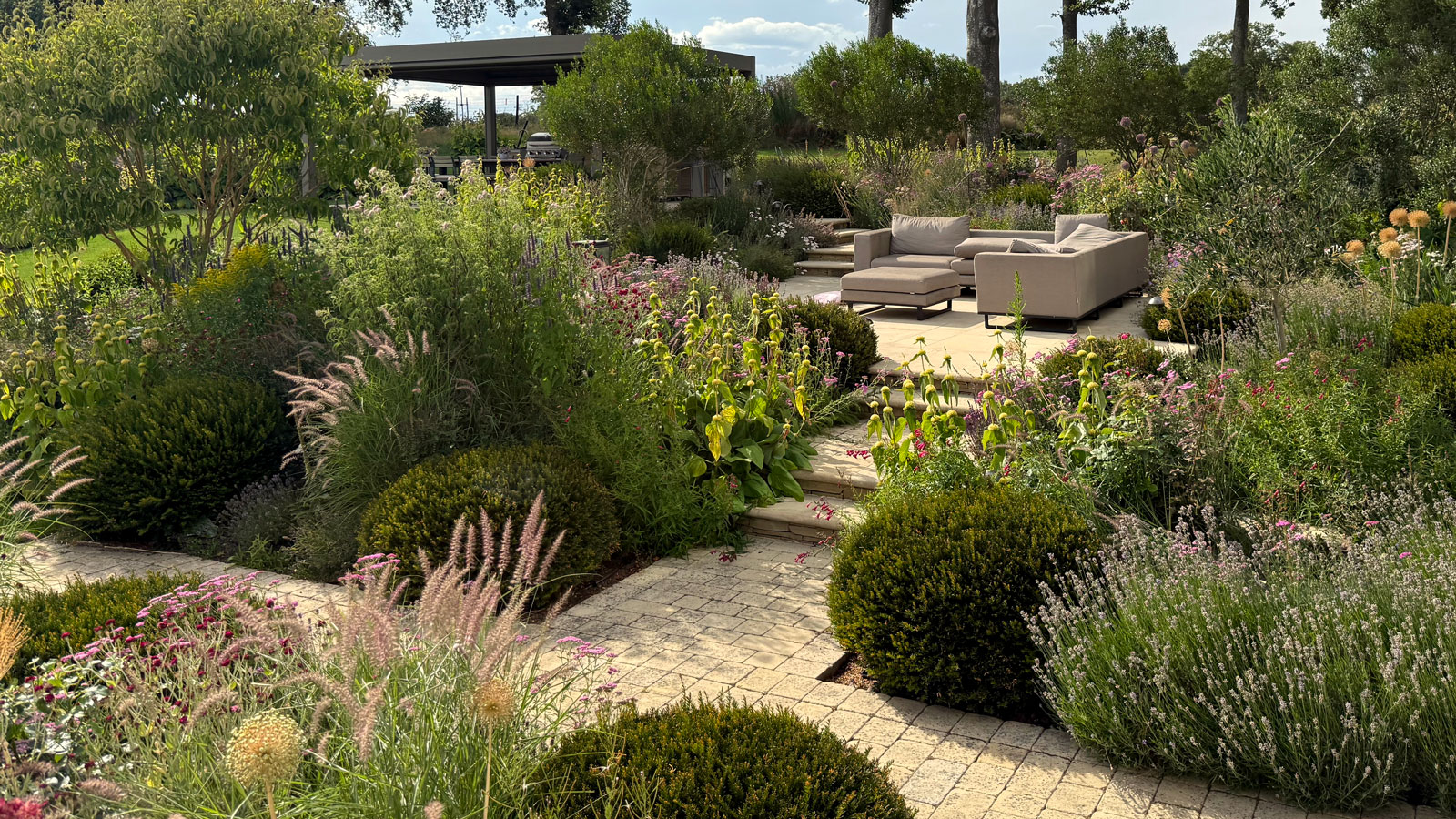 split level garden design featuring planting beds, raised patio area with garden furniture and pergola, all linked by brick paths