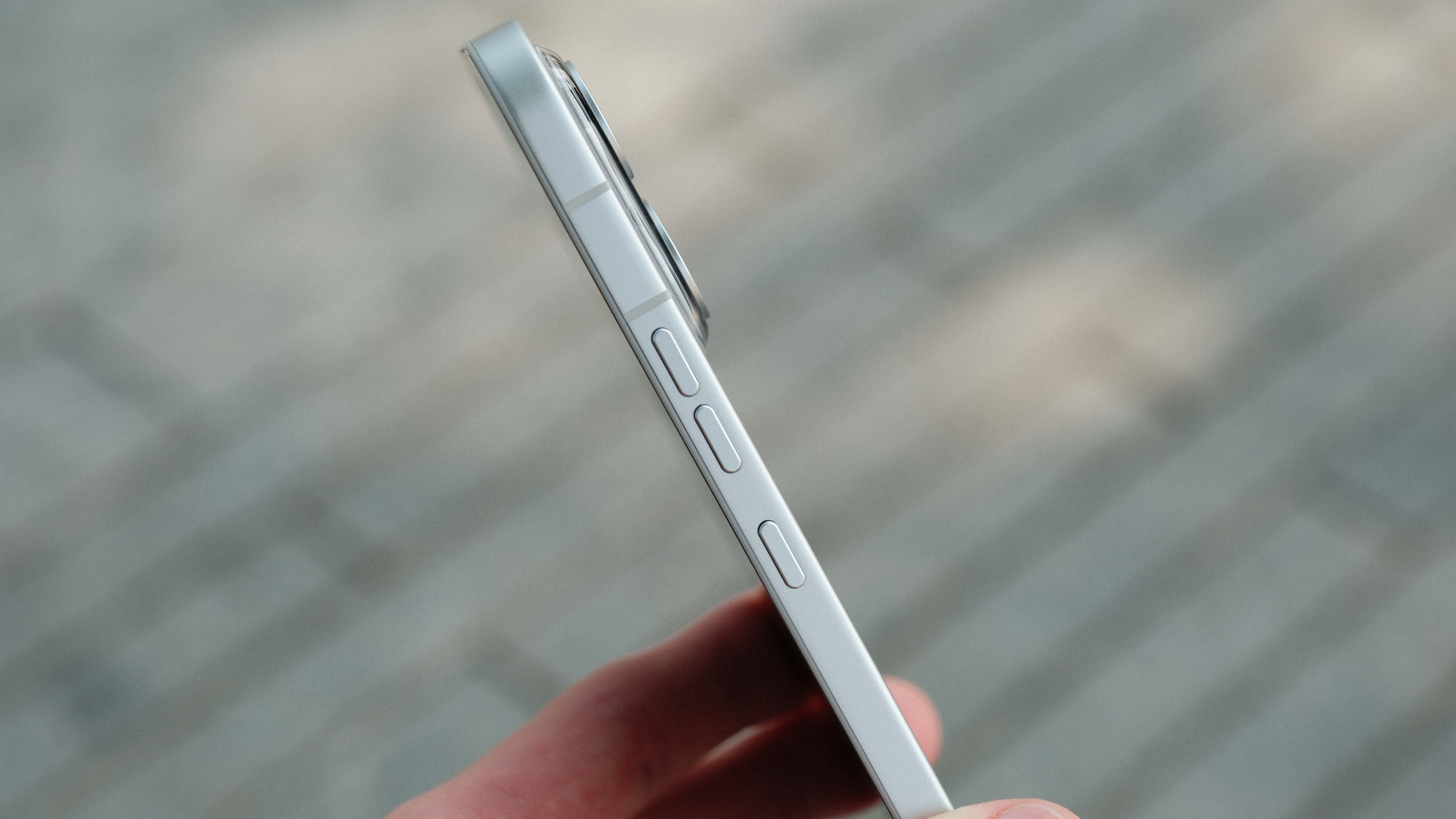 A side view of a smartphone showing three separate physical buttons on the metallic frame: two smaller volume buttons and a larger textured button, set against a blurred outdoor background.
