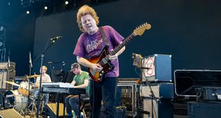 Ty Segall headbangs as he performs live with a Fender Jazzmaster. He wears a purple Dr. Pepper T-shirt.