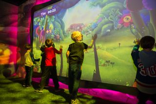 In “Critter Creek”, children can play a game using interactive projections—via Hitachi projectors and a Kinect-based motion capture setup— and tap on Trolls to “invite” them to the dance party.